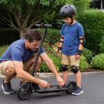 Parent checking the brake on an electric scooter for a helmeted 8-year-old rider