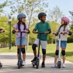 Kids ages 8 to 12 wearing helmets beside electric scooters with adult supervision