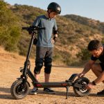 Parent checking the rear brake and tires on an off-road electric scooter for an older teen